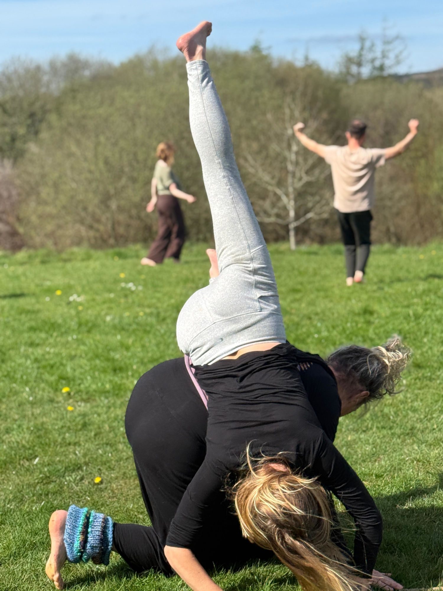 two woment dancing contact improvisation on the grass with 2 dancers in the background