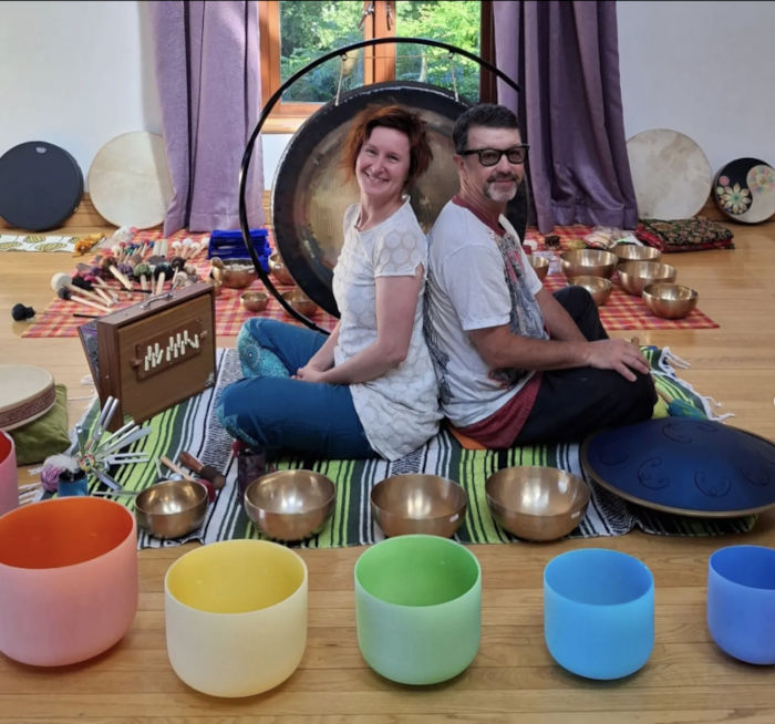 Simone and Nigel seated with singing bowls and assorted sound healing instruments